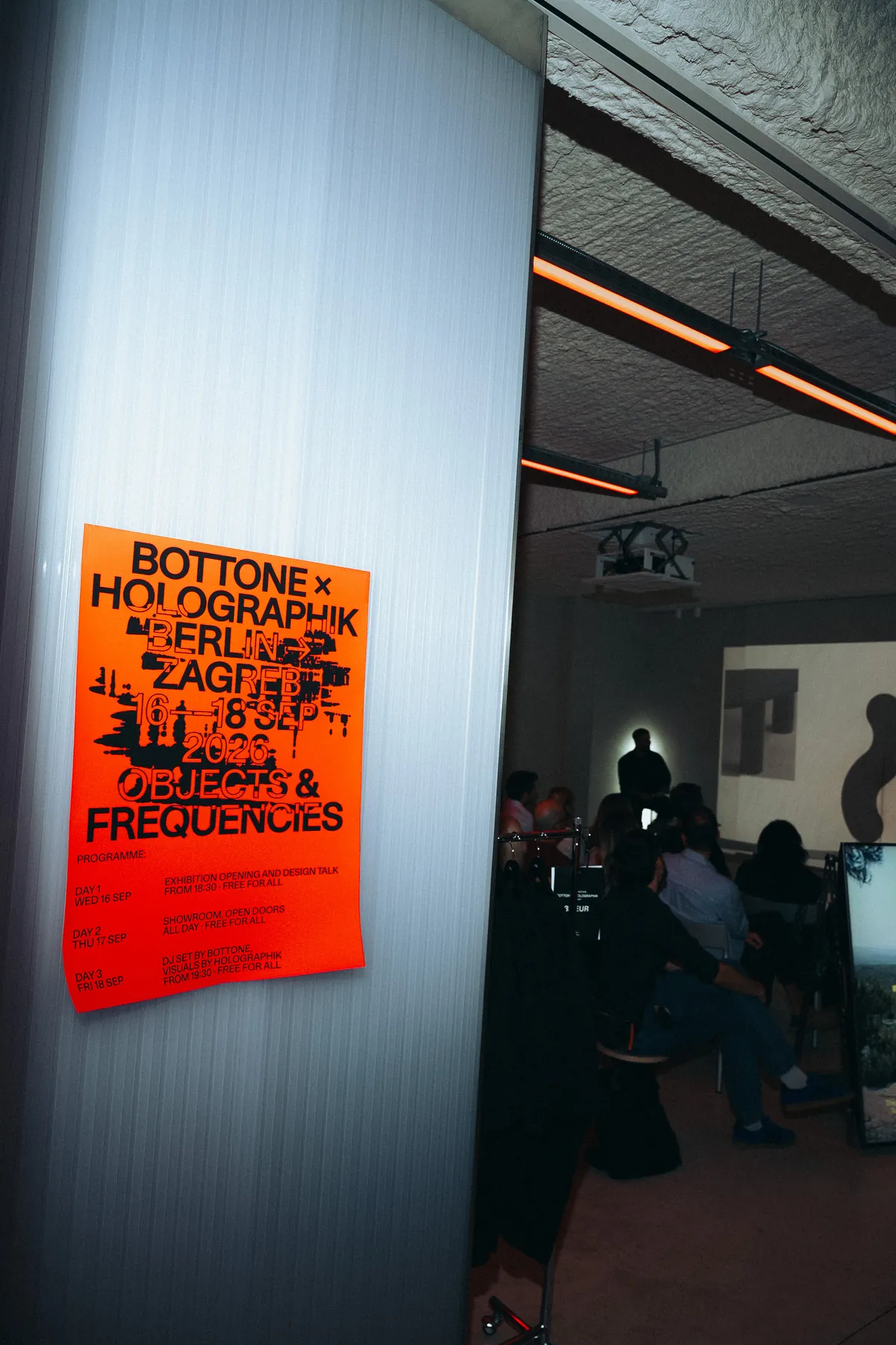 The programme poster beside the seated audience