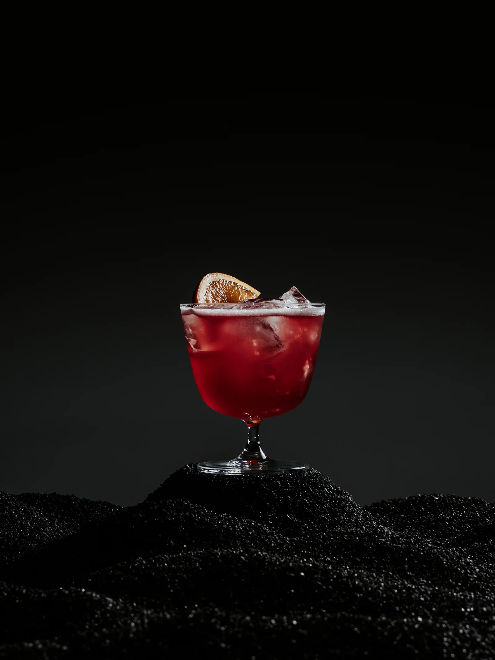 Refine, a Campari and red wine cocktail from the winter menu, on a bed of black sand