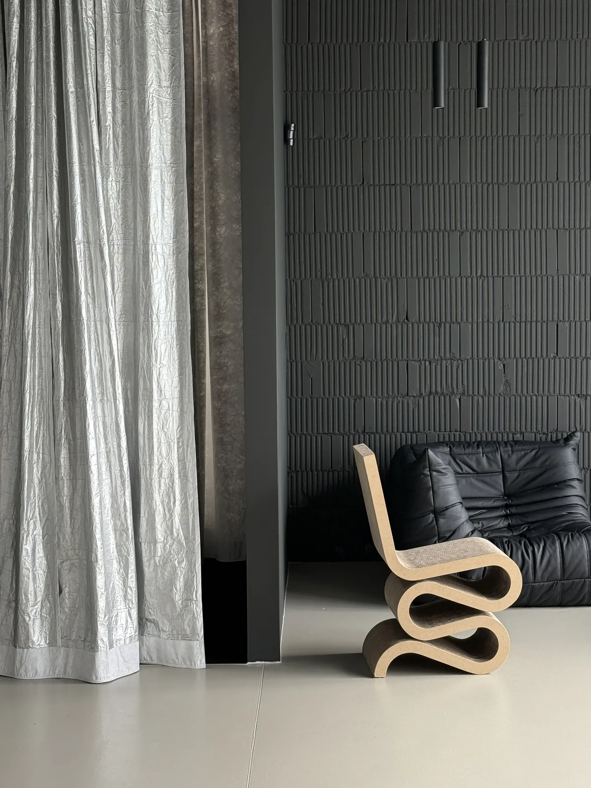 Wiggle Side Chair and a black leather Togo by a silver curtain