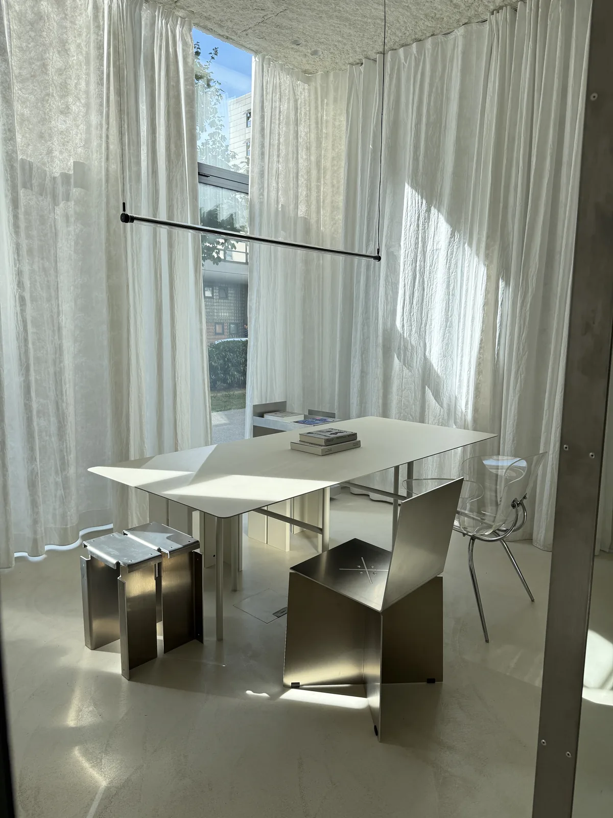 Stainless steel table with stools behind a sheer curtain